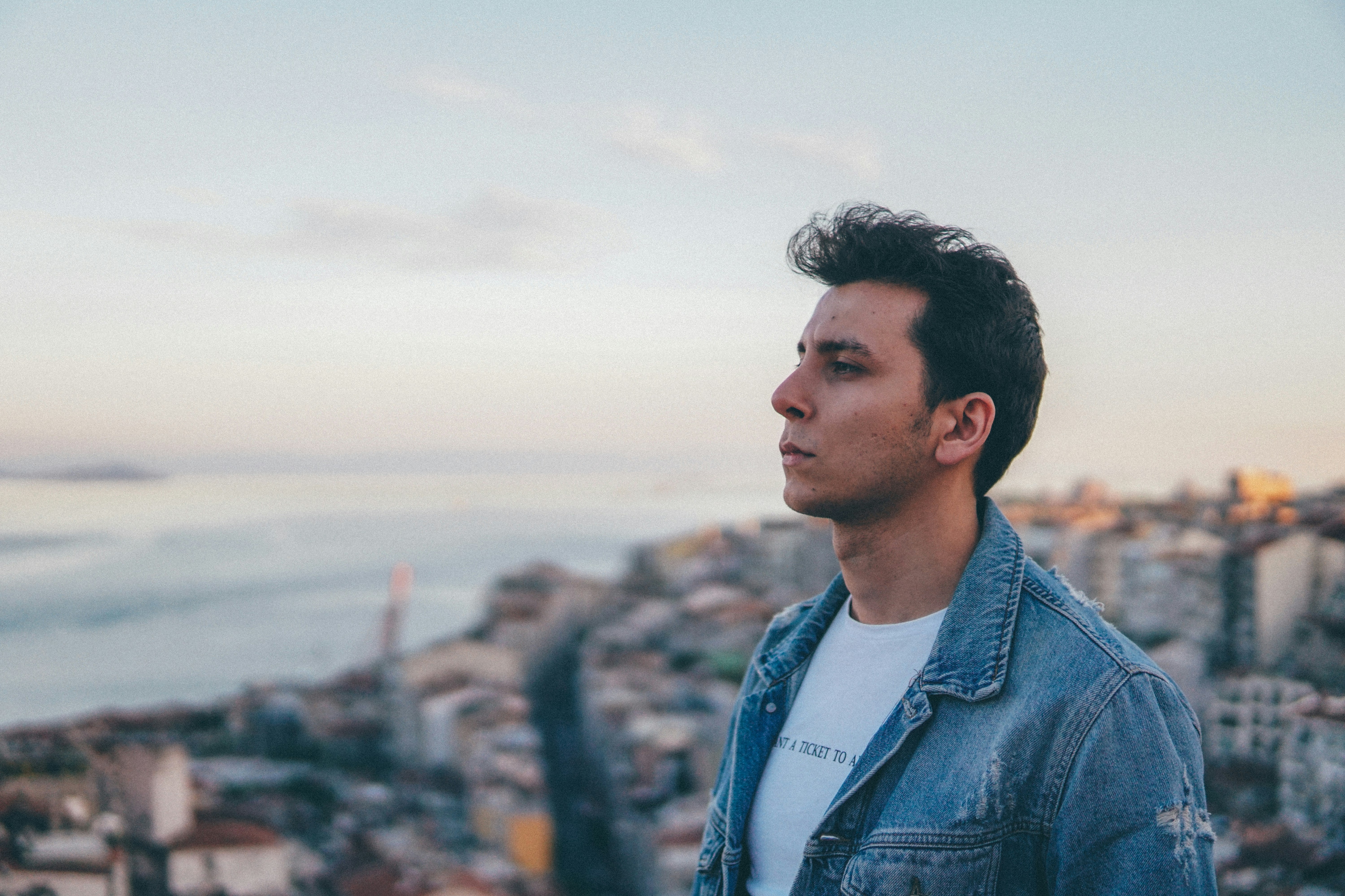 man in blue denim jacket standing on rock during daytime